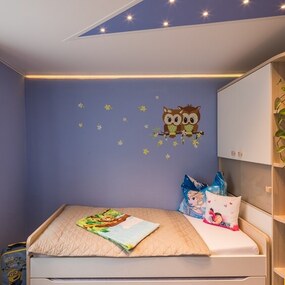 Modern eingerichtetes Kinderzimmer mit gemütlichem Bett, Wandtattoo Eulen und Pflanzen.